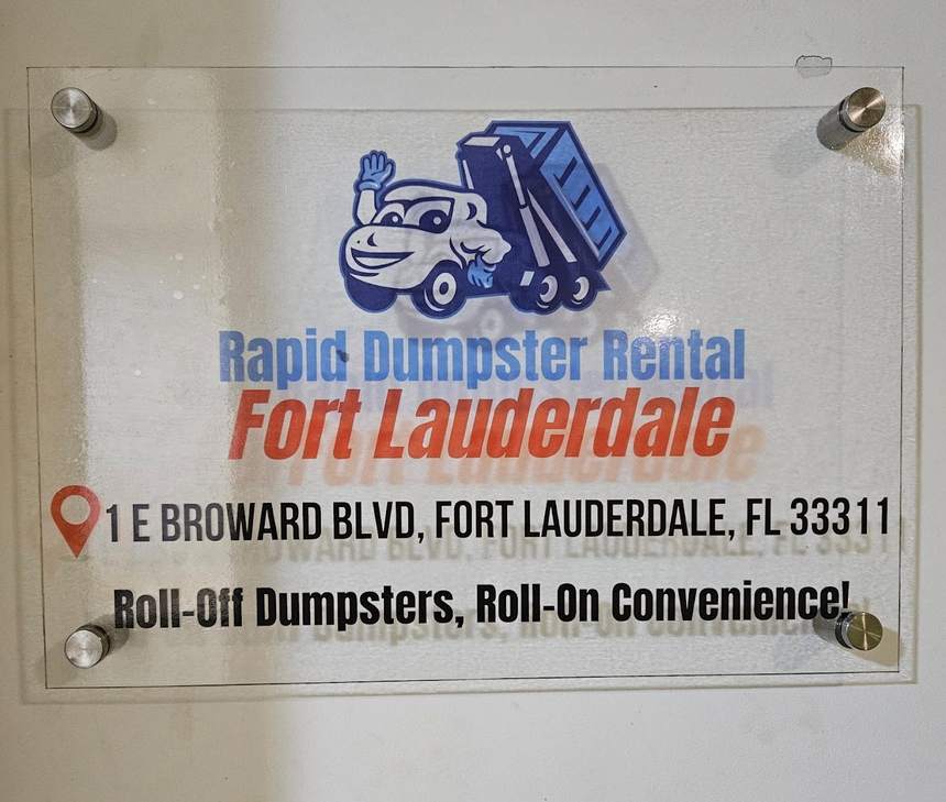 The clear acrylic office sign carrying the Rapid Dumpster Rental Fort Lauderdale logo, the brand name and the street address